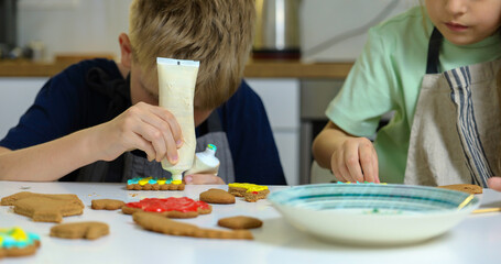 Little boy and girl decorate cookies on table with icing.