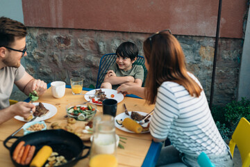 A Caucasian boy doesn’t want to eat his lunch. Family eating together in the backyard