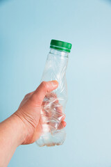Used plastic bottle in human hand on blue paper background. Concept of earth day, zero waste and plastic recycling.