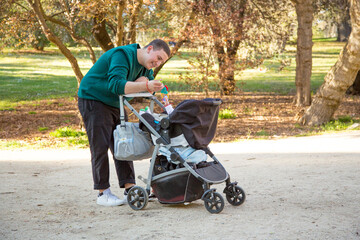 Obraz premium young father playing with his son in his baby carriage in the park