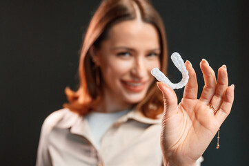 Young woman is standing against black background and holding aligner