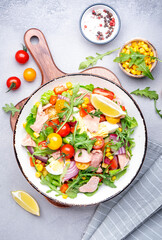Canned tuna salad with cherry tomatoes, red onion, eggs, sweet corn, paprika, lettuce, radicchio and arugula. Gray table background, top view