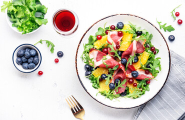 Gourmet salad with smoked duck fillet, fruit and berries, arugula and lettuce, white table background, top view