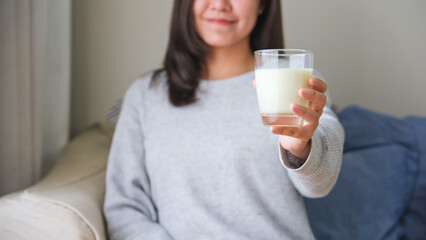 Closeup image of a young woman holding and showing a glass of fresh milk