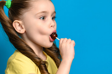 On a blue background, a girl licks a round lollipop close-up
