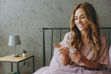 Young woman wear purple t-shirt pajama lying in bed apply hand cream rest relax spend time in...