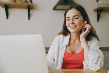 Young happy fun housewife IT woman wears casual clothes earphones hold use working on laptop pc computer listen music eat breakfast cooking food in light kitchen at home alone. Healthy diet concept.