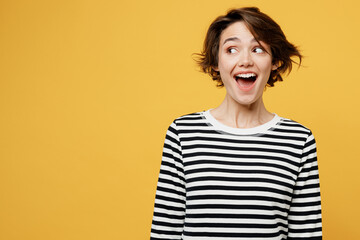 Young surprised happy fun cheerful woman wears casual striped black and white shirt look aside on workspace area mock up isolated on plain yellow color background studio portrait. Lifestyle concept.