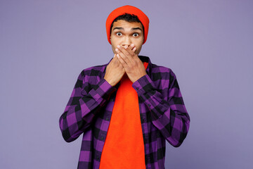 Young shocked scared sad upset man of African American ethnicity wear casual shirt orange hat look camera cover mouth with hands isolated on plain pastel light purple color background studio portrait.