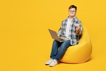 Full body young man with down syndrome wear glasses casual clothes sit in bag chair use mobile cell...