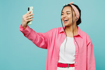 Young woman of African American ethnicity wear pink shirt white t-shirt doing selfie shot on mobile cell phone post photo on social network isolated on plain pastel light blue cyan background studio.