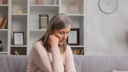 Sad senior woman sitting on the sofa sad because of bad news, problems in the family. Experiences...