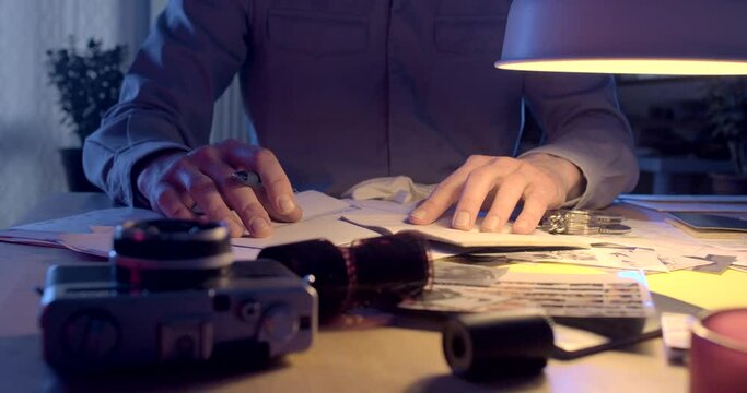 The hands of the investigator control the documents at the table. He examines the negative film at the military evidence. Night work worker. CZ, Kladno, Polska, 8.3.23