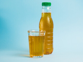 Glass of juice and plastic bottle on blue paper background. Concept of earth day, zero waste and plastic recycling.