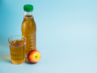 Apple juice drink in plastic bottle and reusable glass cup on blue paper background. Concept of earth day, zero waste and plastic recycling.