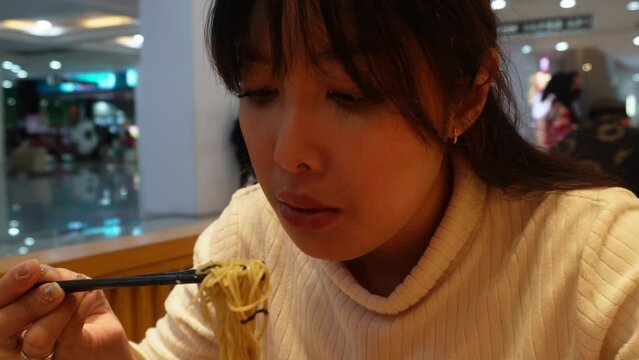 An attractive Asian woman is having dinner at the restaurant, eating ramen or Japanese noodle using chopstick