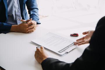 Closeup of Asian female signing car insurance document or lease paper contract or agreement. Buying or selling new or used vehicle with car keys on table.