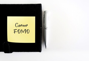 On copy space white background - Yellow note on black notebook with text written CAREER FOMO, fear...
