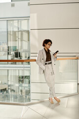 Vertical image of young businesswoman reading message on her smartphone while standing in office...