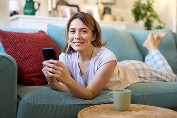 Happy woman text messaging on mobile phone while relaxing in the living room