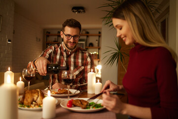 Fototapeta na wymiar Beautiful couple having romantic dinner with candles and red wine at home