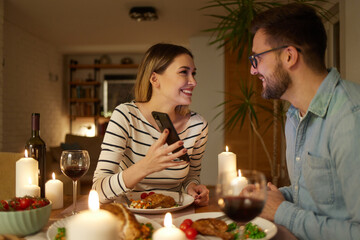 Fototapeta na wymiar Happy couple enjoying food and wine while surfing the net on smart phone