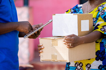 African Postal Delivery Man records receipt details of shipped cardboard box parcel with digital...