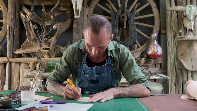 4K, Close-up handcrafted leather worker sits farts cowhide with cutter according pattern drawn on leather, meticulous for beautiful sharp focus, in order make cow leather good piece work.