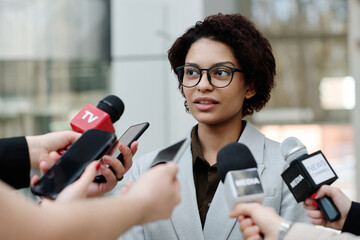 Young businesswoman in eyeglasses giving an interview at business conference, she talking to...