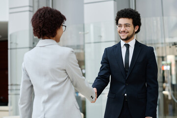 Young business people in formalwear shaking hands and greeting each other before meeting