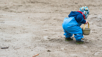 A young child playing in sand with a bucket in his hand