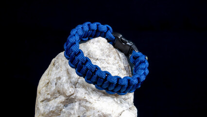 Braided paracord bracelet on a stone, on a black background. Handmade, creative design.