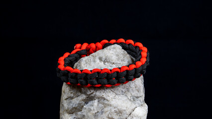 Braided paracord bracelet on a stone, on a black background. Handmade, creative design.