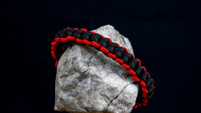 Braided paracord bracelet on a stone, on a black background. Handmade, creative design.