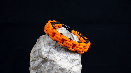 Braided paracord bracelet on a stone, on a black background. Handmade, creative design.