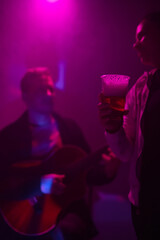 Woman holding a plastic beer cup with a musician playing guitar in the club background.