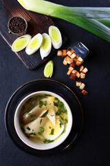 Fresh fish soup in a bowl on a black background, top view. White bread crackers. White fish soup. Transparent broth. A healthy dish.Lean menu.Vertical photo.Space for copying.He was lying flat.