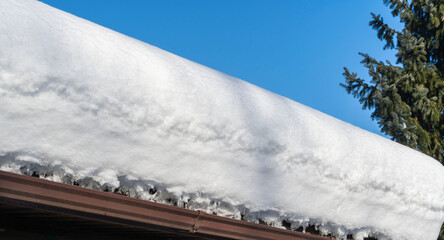 Fragments of roof of country house on sunny winter day after heavy snowfall. Snowdrifts lie on metal roof. Close-up. Drains are clogged with snow.