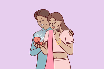 Indian man surprises wife with box of jewelry or engagement ring as token of love and devotion. Guy and girl in Indian national costumes during romantic date or engagement ceremony