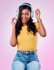 Music, headphones and excited Indian woman dance on pink background listening to track, audio and radio. Relax, happy and isolated girl streaming song for dancing, chilling and happiness in studio