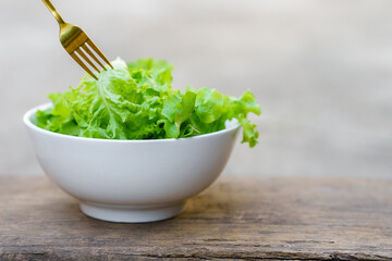 A fork that picks up salad from a white bowl on a wooden background. Healthy food concept.