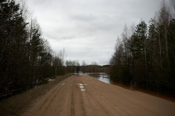 Naklejka premium Flooded dirt road by spring floods. A flooded bridge overflowing the banks of the river.