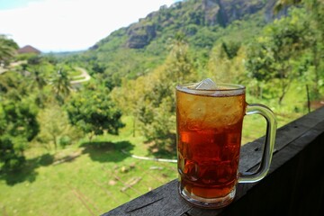 Es teh or Ice Tea in a glass on wooden rails on a summer day at the hills. Bokeh background.