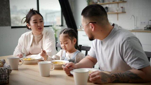 Asian Family Eats Breakfast At Home. Little girl eating corn flakes with her mom and dad. Lovely family happy together. Handheld Camera.
