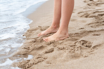 Bare feet of a teenage boy on the sandy shore at the edge of the surf