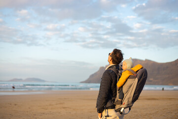 Father rising hands to the sky while enjoying pure nature carrying his infant baby boy son in...