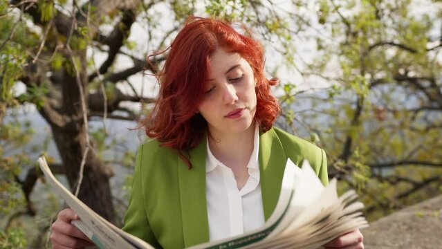 Red hair businesswoman reading newspaper under the tree