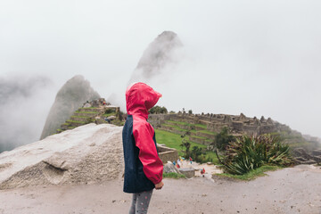 Girl with jacket and hood observing the ruins of Machu Picchu