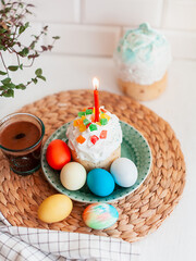Easter homemade cake with marmalade and candied fruits, which is decorated with a candle on top, stands next to colored Easter eggs