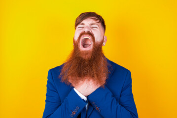 red haired man wearing blue suit over yellow studio background shouting suffocate because painful...